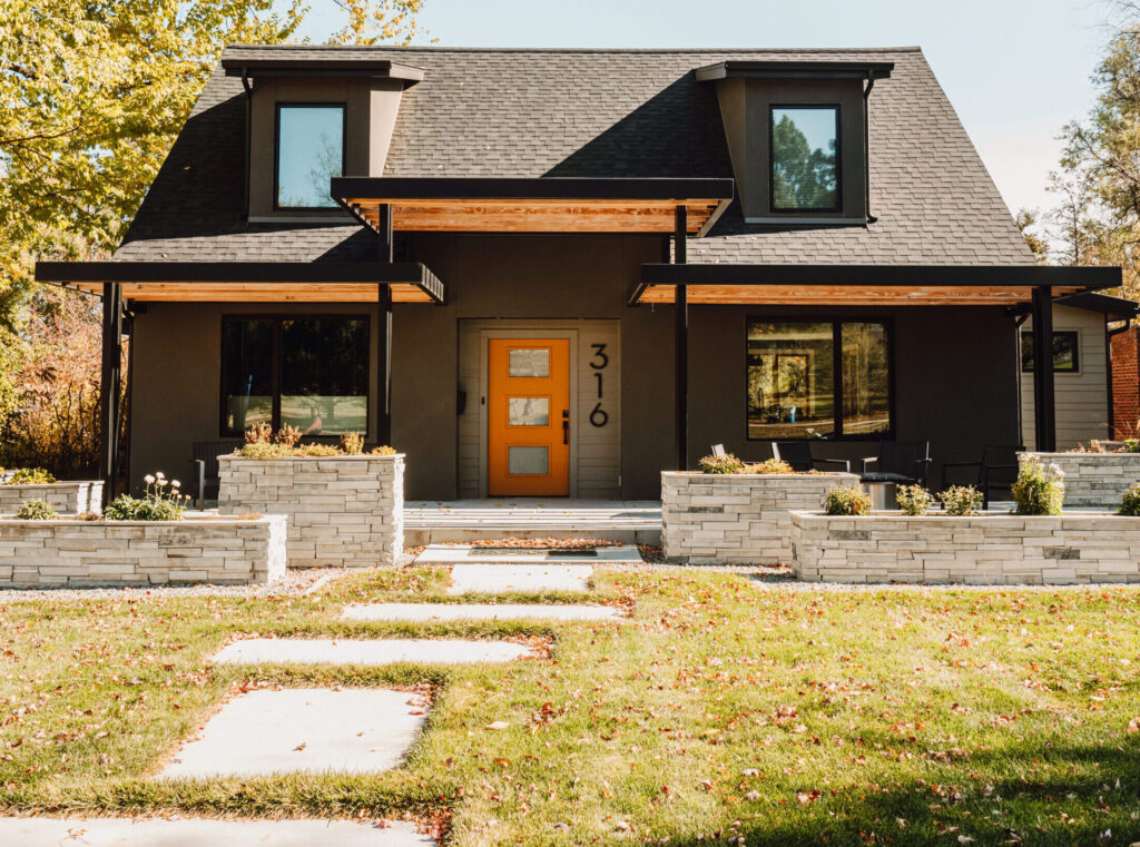 Exterior rendering of a mid-century modern whole home remodel. The house showcases clean lines, minimalist design, and a flat roof characteristic of mid-century architecture. Large windows flood the interior with natural light, while a sleek entrance door adds to the modern aesthetic. The landscaping is kept simple and geometric, complementing the home's style. Overall, the remodel seamlessly combines retro charm with contemporary updates, creating a stylish and functional living space.