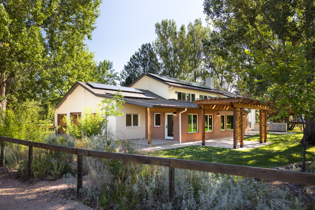 The exterior of the home features a charming brick addition that seamlessly blends with the original structure, enhancing the English countryside aesthetic. A rebuilt wooden pergola stands over the expanded stone patio, creating a cozy outdoor living space. The patio, made from natural stone, stretches out into the surrounding countryside, offering ample space for seating and outdoor gatherings. The home's soft, earthy tones and mixed materials harmonize with the scenic Fort Collins landscape, combining rustic elegance with modern comfort.