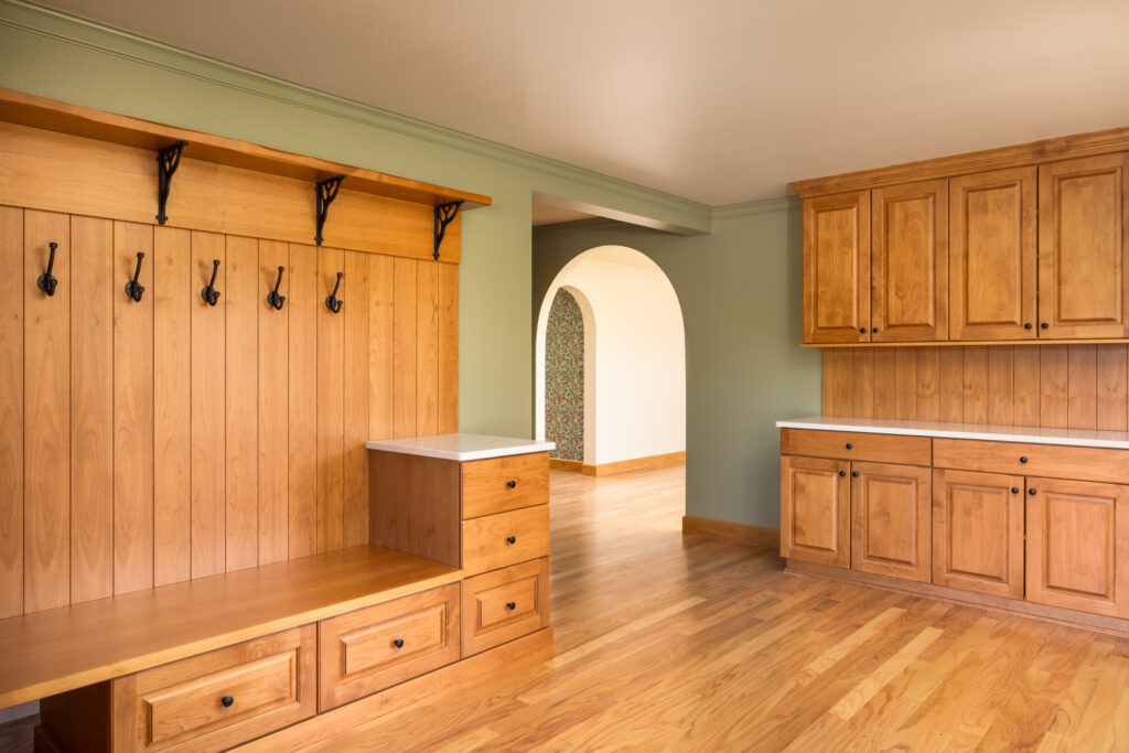 The mudroom is designed for both practicality and style, featuring rustic wooden hooks, a sturdy bench for seating, and storage cubbies. The space is finished with durable wood flooring and a soft color palette that ties it into the home’s overall aesthetic.
